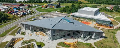 Katuseremont Rae vallas, ülalt vaade uue hoone nurgelisele hallile katusele ja kõrval asuvale suurele lamekatusega hallile, suurel lamekatusel teeb droon kaks ringi, esimese kogu katuse ülevaatefotoks ja teise madalalt iga läbiviigu kohalt.