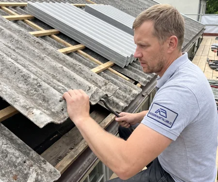 Katusemeister kangutab katuselt vana lainelist eterniitplaati, taga virnas uued profiilplekid, eterniidi asemele tulev plekk tellitakse tehasest iga katuse mõõtu lõigatuna.