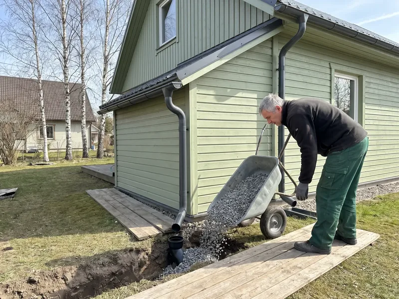 Hallipäine töömees kallutab kärust kruusa kaevikusse rohelise puitmaja kõrval, seinal uus tumehall allavoolutoru, imbväljakusse läheb ainult pestud kruus, sest pesemata kruusa peenosa ummistab imbumise.