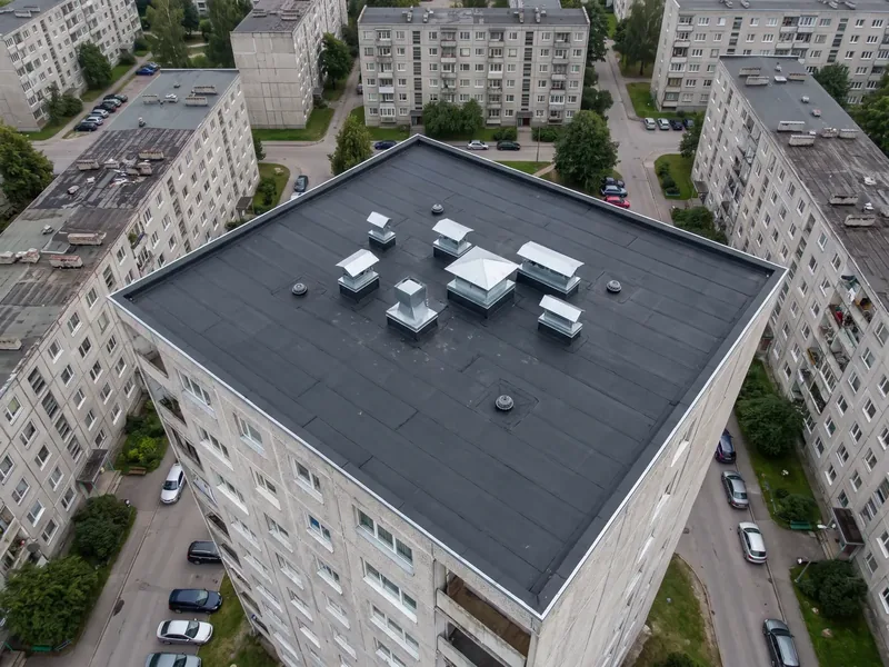 Droonifoto paneelmaja uuest mustast lamekatusest ventilatsioonihoodidega, SBS-rullide laotamine algab katuse madalaimast kohast, nii et iga ülekate jääb vee voolusuunas.